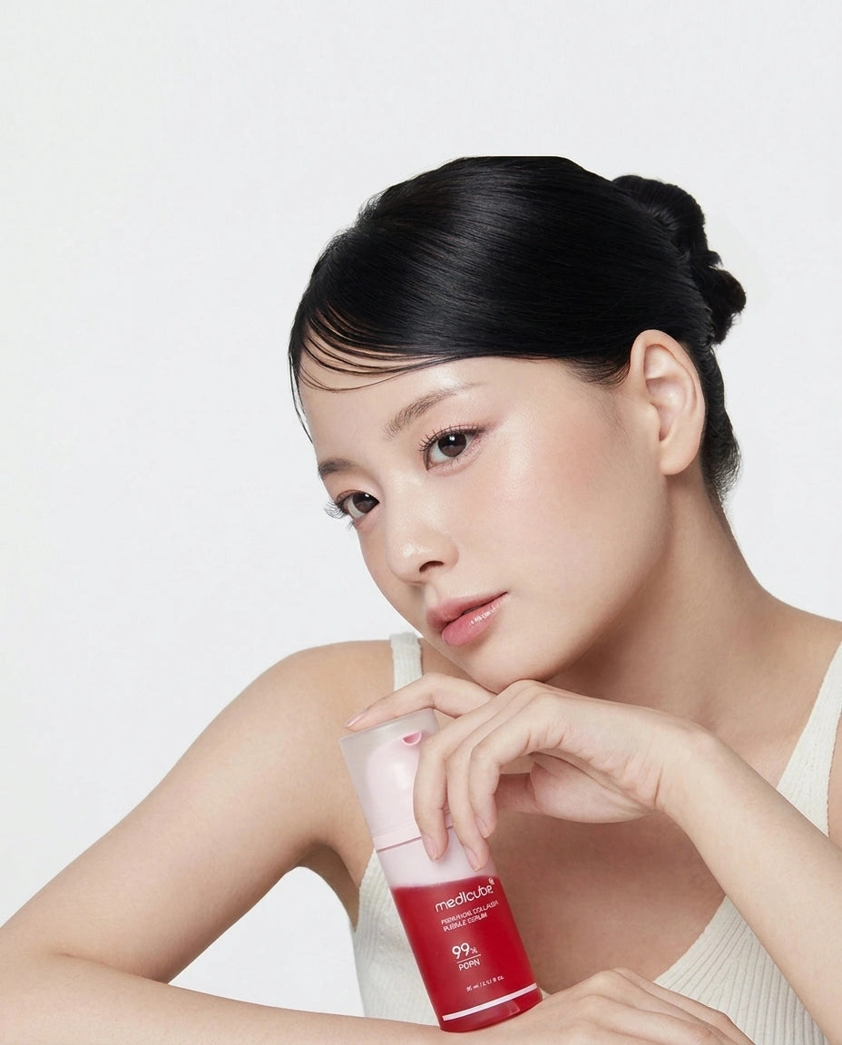 A woman with her hair in a bun holds a red and white miheera skincare bottle against a clean white background.