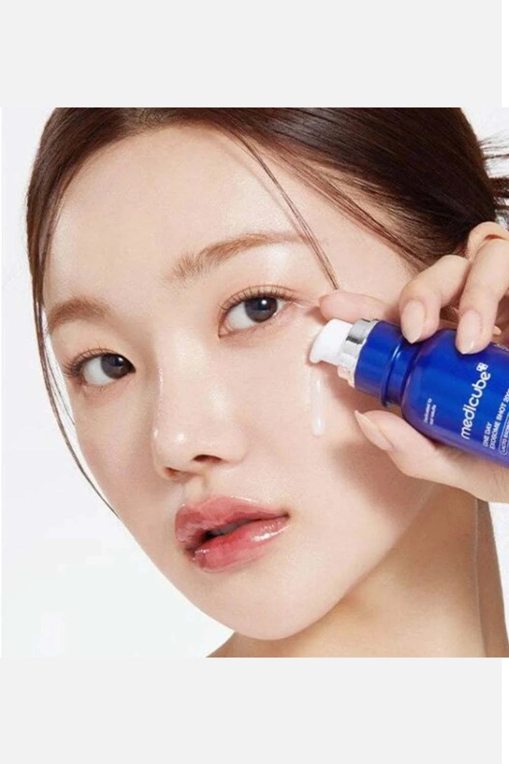 Person applying a blue skincare serum to their face with a white background