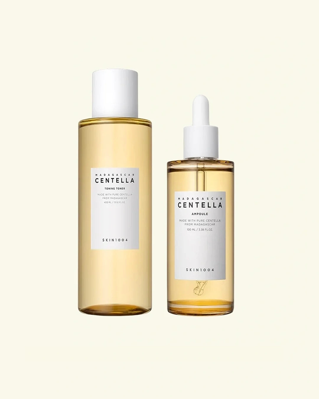 Two De'Nique skincare bottles on a light cream background: a larger clear bottle with pale golden liquid and a white cap, and a smaller dropper bottle with the same pale golden liquid and a white label.