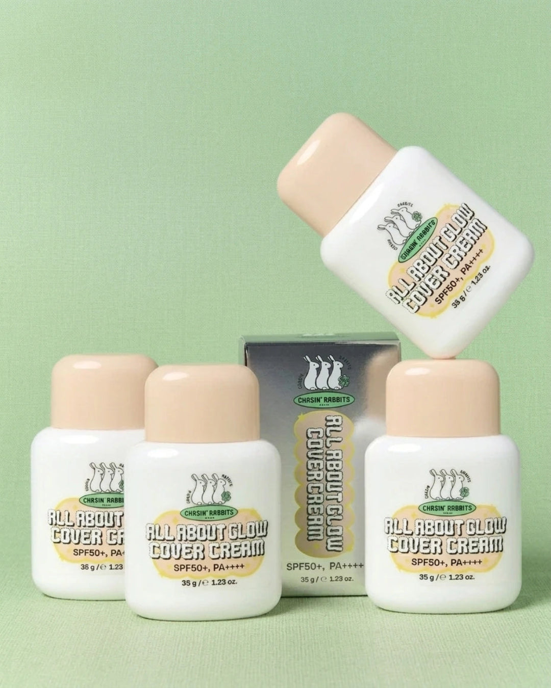 Four white bottles of Chown Brand All About Glow Cover Cream with beige caps and a matching box, arranged on a light green background.