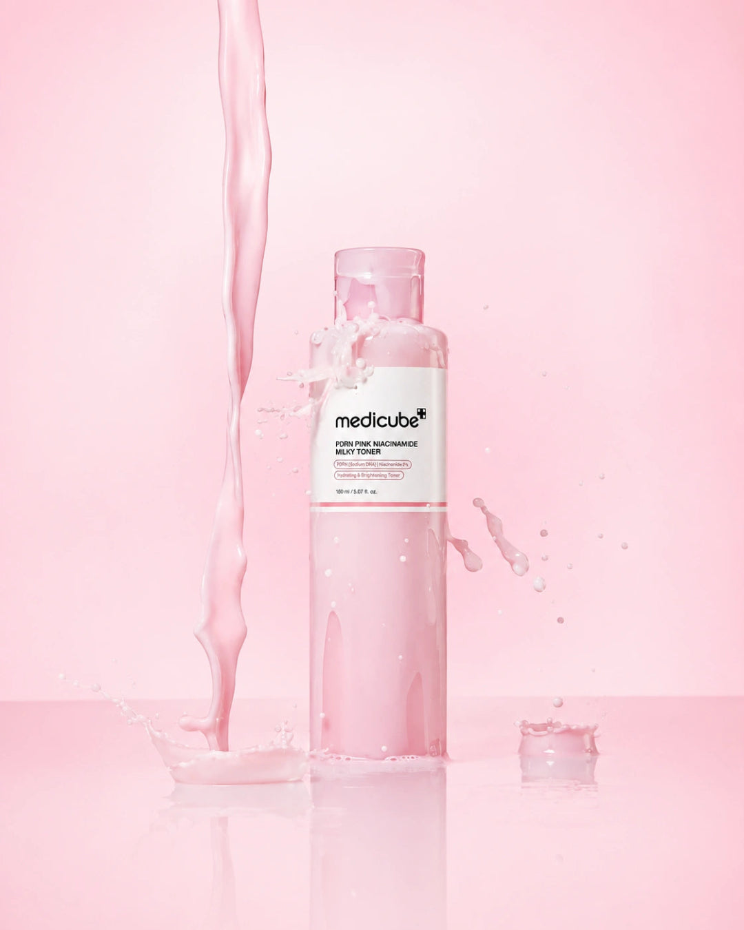 A bottle of medicube Ultra Fine Emulsion Clean Toner with a pink liquid inside, set against a pink background with a pink liquid splash and droplets.