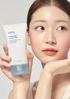 Woman holding a DPPR Hyalcube cream tube against a neutral background