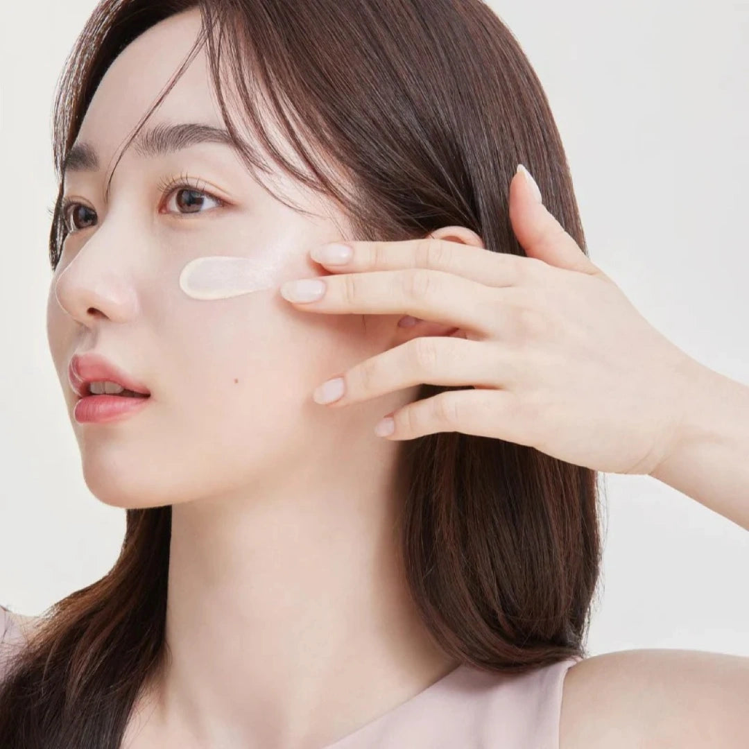 Woman applying cream to her face with a neutral background