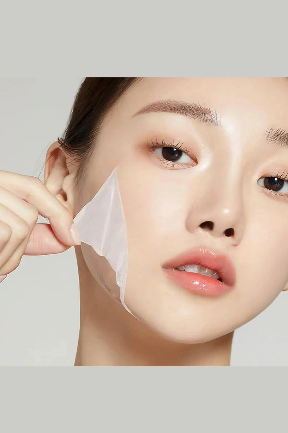 Person applying a skincare patch to their face against a neutral background